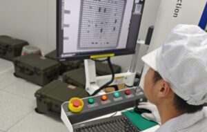 Worker in white cap inspecting components on a monitor at a drone jammer production facility